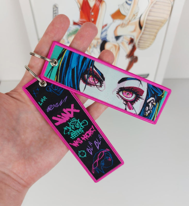 Arcane Jinx embroidered jet tag keychain featuring neon graffiti art on a premium heavy-duty woven black fabric strap.