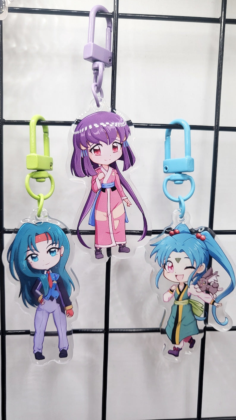 Exclusive Tenchi Muyo acrylic keychain featuring double-sided designs of Ryo-Ohki, Tenchi, Sasami, Ryoko Hakubi, Washu, Ayeka, Mihoshi, and Kiyone. Vibrant, scratch-resistant colors with a glitter epoxy coating for a standout look. Perfect for accessorizing backpacks, lanyards, and Ita bags. Durable silver D-clasp for long-lasting use. A must-have collectible and a perfect gift for Tenchi Muyo and anime fans!