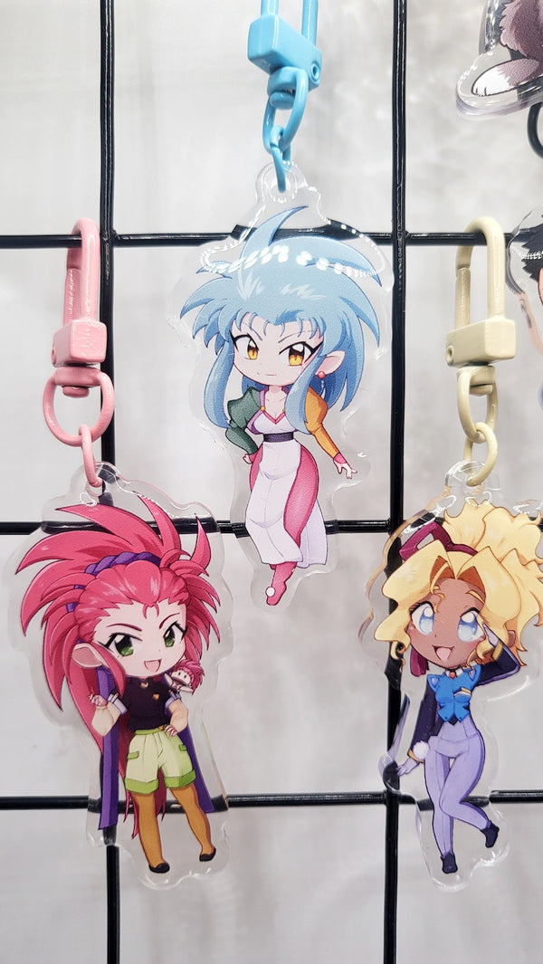 Exclusive Tenchi Muyo acrylic keychain featuring double-sided designs of Ryo-Ohki, Tenchi, Sasami, Ryoko Hakubi, Washu, Ayeka, Mihoshi, and Kiyone. Vibrant, scratch-resistant colors with a glitter epoxy coating for a standout look. Perfect for accessorizing backpacks, lanyards, and Ita bags. Durable silver D-clasp for long-lasting use. A must-have collectible and a perfect gift for Tenchi Muyo and anime fans!