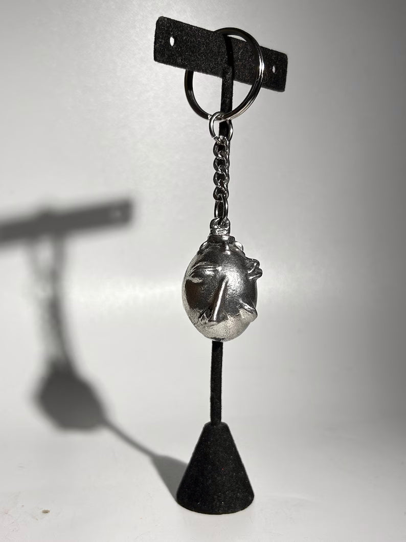 Handcrafted Behelit Keychain – Cast from solid, lead-free 97LF alloy pewter with a stainless steel chain and iron split ring. Unique, hand-finished charm with subtle imperfections, symbolizing dark fantasy and artistry. 4.25-inch (11 cm) drop length, perfect for Berserk fans, collectors, and admirers of symbolic accessories. Durable and distinctive design for daily use or display.